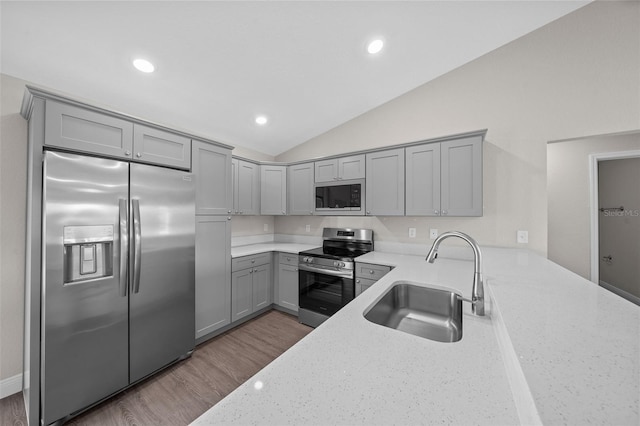 kitchen with sink, built in appliances, vaulted ceiling, light stone countertops, and light hardwood / wood-style floors