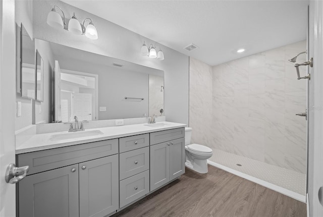 bathroom with hardwood / wood-style flooring, tiled shower, vanity, and toilet