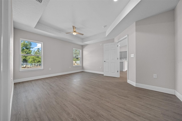 empty room with ceiling fan, a tray ceiling, and dark hardwood / wood-style flooring