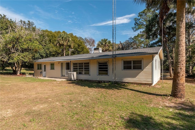 rear view of house with central AC unit and a lawn