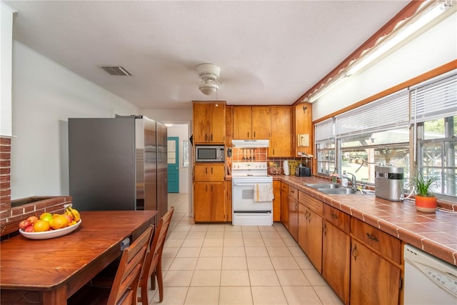 kitchen with appliances with stainless steel finishes, tile countertops, sink, backsplash, and light tile patterned floors