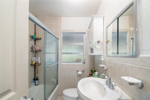 full bathroom featuring toilet, combined bath / shower with glass door, sink, and tile walls