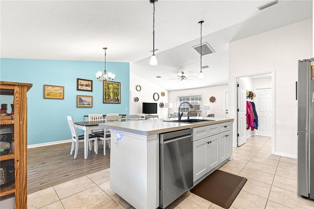 kitchen with decorative light fixtures, sink, white cabinets, stainless steel appliances, and a center island with sink