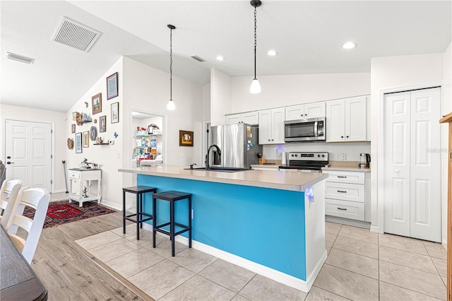 kitchen with appliances with stainless steel finishes, white cabinetry, a kitchen breakfast bar, hanging light fixtures, and a center island with sink