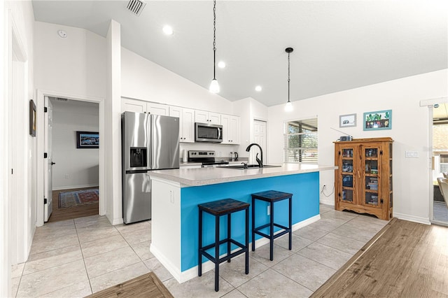 kitchen featuring a breakfast bar area, appliances with stainless steel finishes, white cabinetry, a center island with sink, and decorative light fixtures