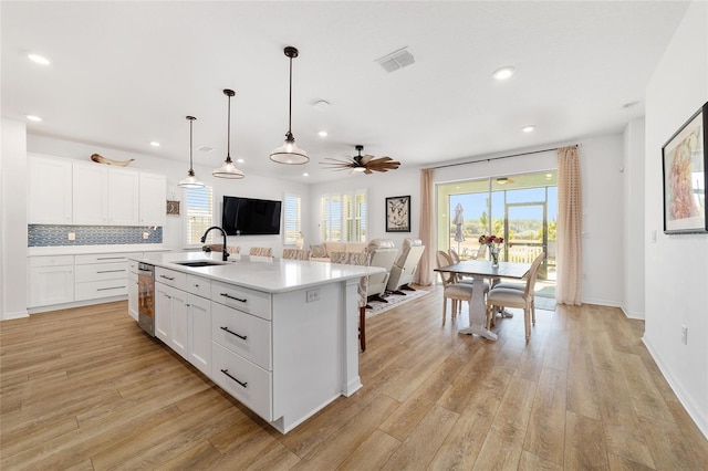 kitchen featuring white cabinetry, light hardwood / wood-style floors, hanging light fixtures, and a center island with sink