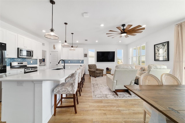 kitchen featuring pendant lighting, a breakfast bar area, white cabinetry, stainless steel appliances, and a large island with sink