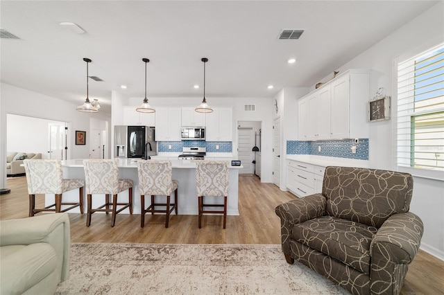 kitchen with pendant lighting, white cabinetry, stainless steel appliances, and a kitchen island with sink