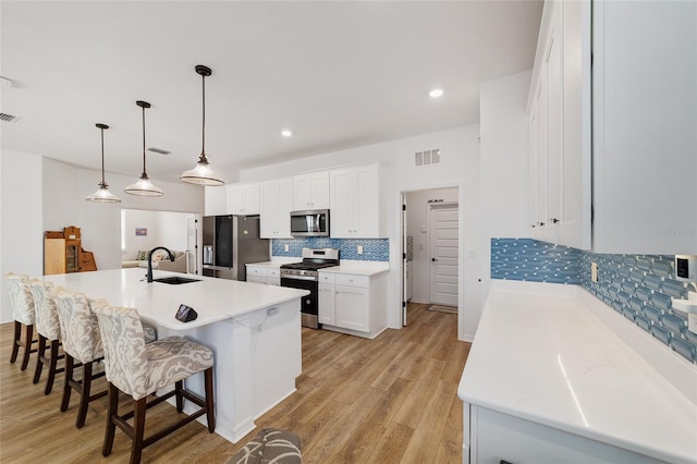 kitchen with pendant lighting, sink, white cabinetry, stainless steel appliances, and a center island with sink