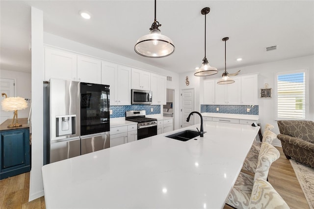 kitchen featuring sink, white cabinetry, decorative light fixtures, stainless steel appliances, and a kitchen island with sink