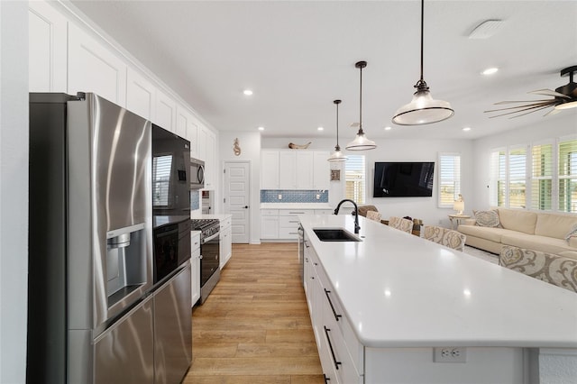 kitchen featuring appliances with stainless steel finishes, decorative light fixtures, white cabinetry, sink, and a large island with sink