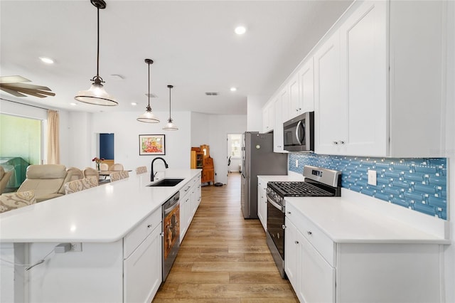 kitchen with sink, appliances with stainless steel finishes, a kitchen island with sink, white cabinetry, and decorative light fixtures