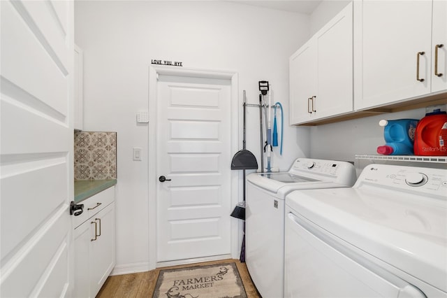 washroom featuring cabinets, washing machine and clothes dryer, and light hardwood / wood-style flooring