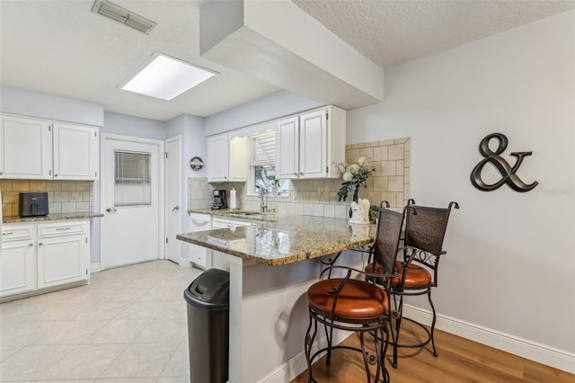 kitchen with white cabinetry, a breakfast bar area, light stone countertops, and kitchen peninsula