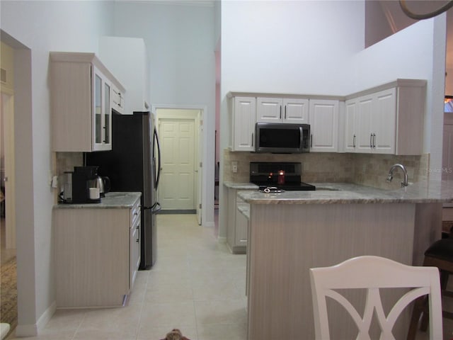 kitchen with light tile patterned floors, stainless steel appliances, a high ceiling, and kitchen peninsula