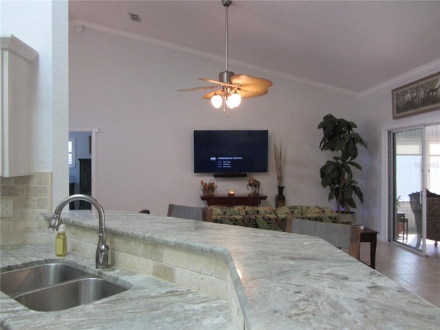 kitchen with sink, ceiling fan, tile patterned flooring, ornamental molding, and light stone countertops