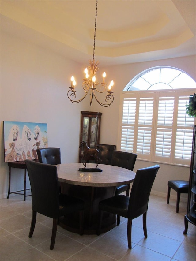 dining space featuring a notable chandelier, a raised ceiling, and tile patterned floors