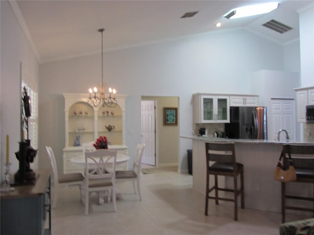 dining space with hanging light fixtures, a kitchen breakfast bar, white cabinets, ornamental molding, and an inviting chandelier