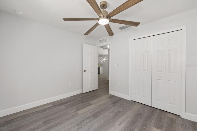 unfurnished bedroom with a ceiling fan, visible vents, wood finished floors, baseboards, and a closet