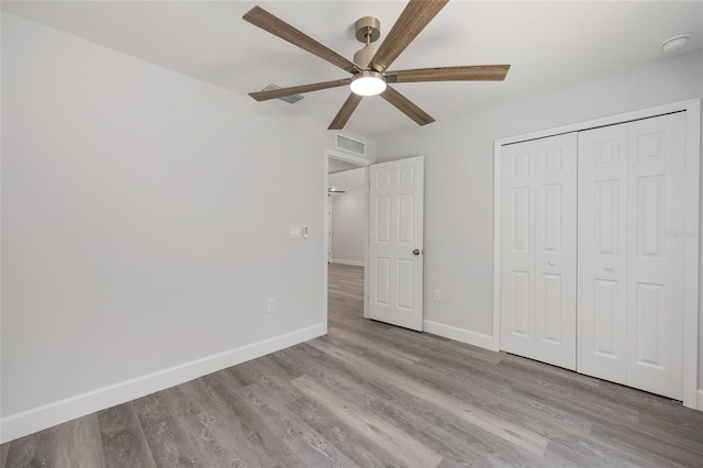 unfurnished bedroom featuring visible vents, a closet, wood finished floors, baseboards, and a ceiling fan