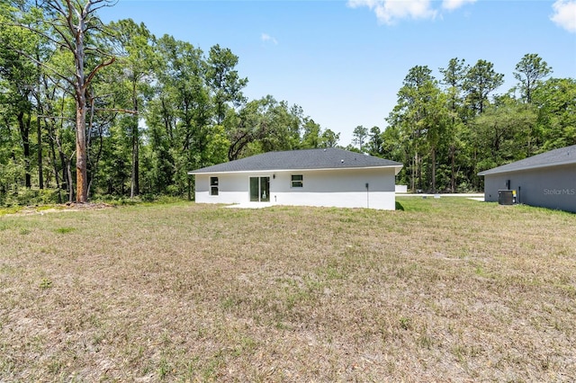 back of house featuring a lawn, central air condition unit, and stucco siding