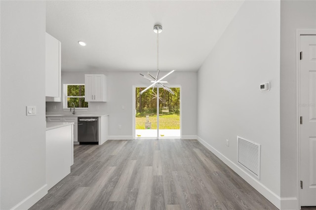 unfurnished dining area with baseboards, visible vents, a sink, and light wood-style floors