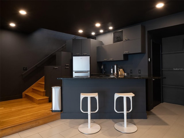 kitchen featuring dark stone countertops, a breakfast bar area, kitchen peninsula, and white refrigerator