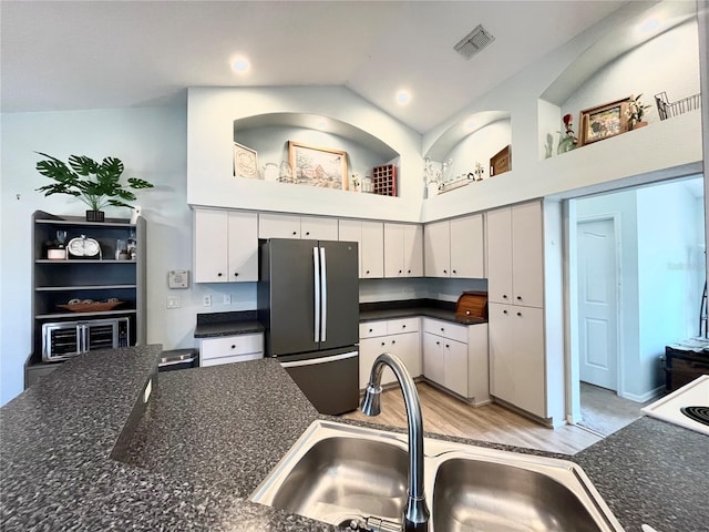 kitchen with high vaulted ceiling, sink, white cabinets, stainless steel fridge, and light wood-type flooring