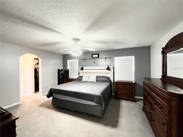 carpeted bedroom with ceiling fan, a textured ceiling, and a walk in closet