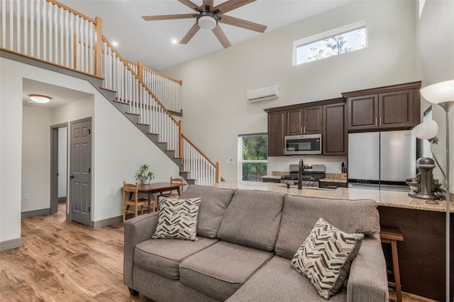 living room with an AC wall unit, a towering ceiling, sink, ceiling fan, and light hardwood / wood-style floors