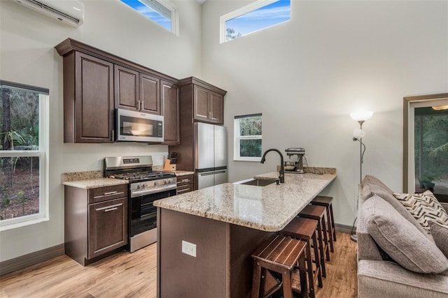 kitchen featuring dark brown cabinetry, sink, light stone counters, an AC wall unit, and stainless steel appliances