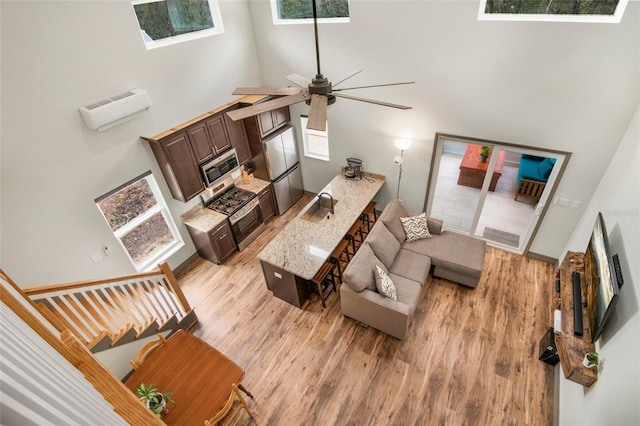 living room featuring sink, a wall mounted AC, a towering ceiling, ceiling fan, and light hardwood / wood-style floors