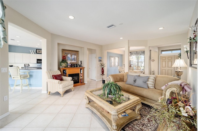 living area with light tile patterned floors, a glass covered fireplace, visible vents, and recessed lighting