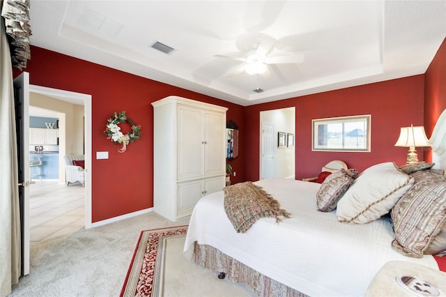 bedroom featuring light carpet, visible vents, a tray ceiling, and baseboards