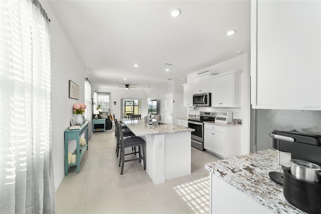 kitchen with an island with sink, white cabinetry, a kitchen breakfast bar, light stone counters, and stainless steel appliances