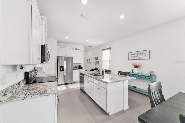 kitchen featuring sink, appliances with stainless steel finishes, white cabinetry, light stone countertops, and an island with sink