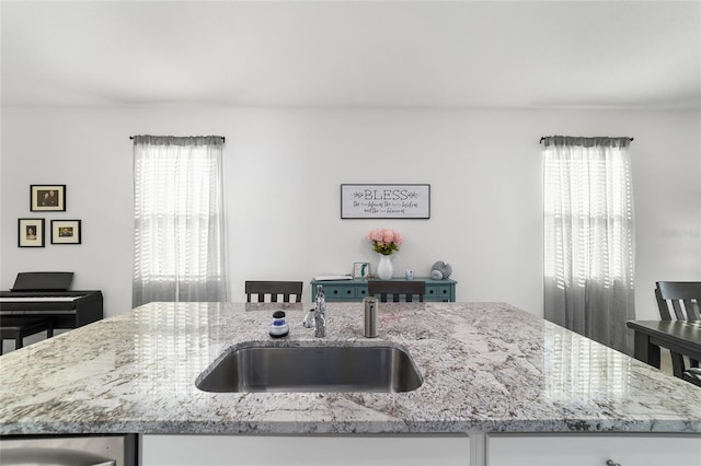 kitchen featuring light stone countertops, sink, a center island with sink, and a wealth of natural light