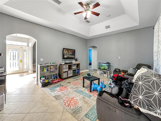 living room featuring light tile patterned floors, a raised ceiling, ceiling fan, and a high ceiling