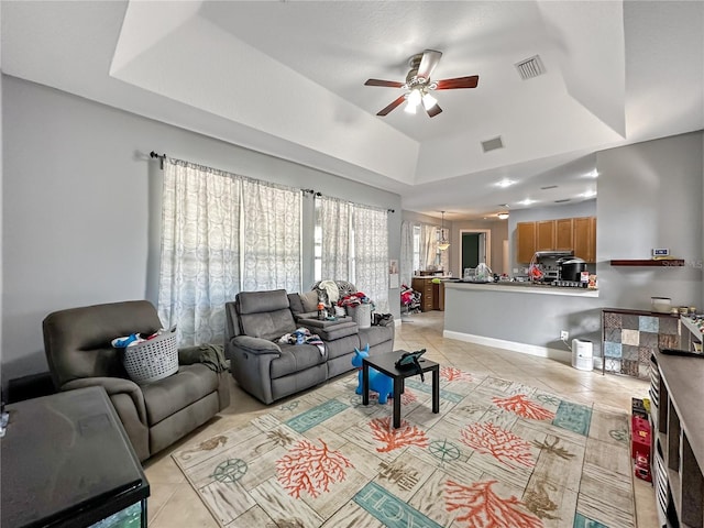 living room with light tile patterned floors, a tray ceiling, and ceiling fan