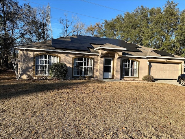 ranch-style home featuring a garage, a front lawn, and solar panels