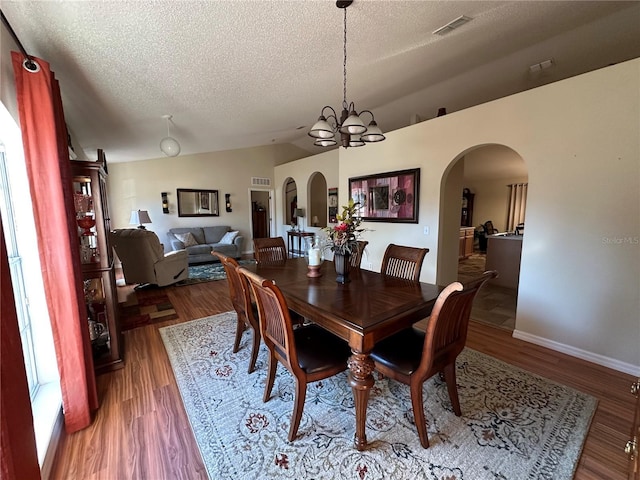 dining room with an inviting chandelier, lofted ceiling, dark hardwood / wood-style floors, and a textured ceiling