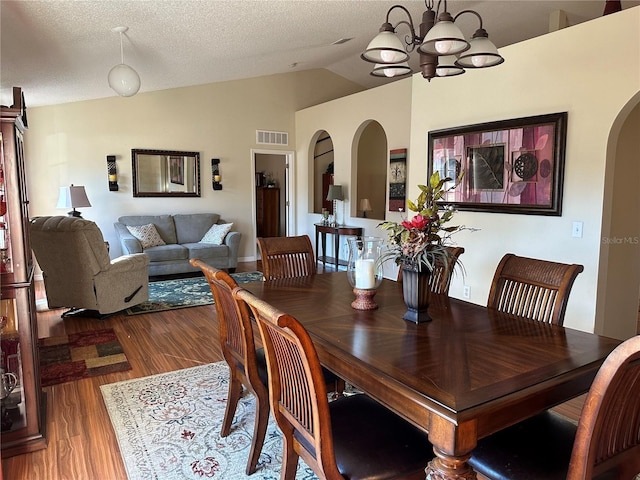 dining area featuring hardwood / wood-style flooring, an inviting chandelier, vaulted ceiling, and a textured ceiling