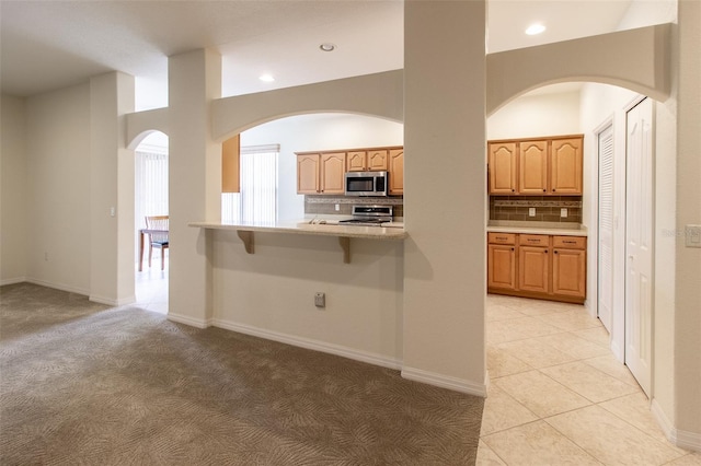 kitchen with a breakfast bar, light brown cabinets, kitchen peninsula, and appliances with stainless steel finishes