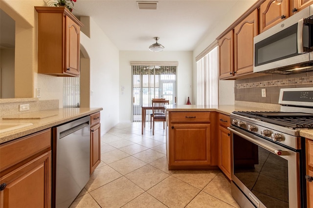 kitchen featuring tasteful backsplash, light tile patterned floors, light stone counters, kitchen peninsula, and stainless steel appliances