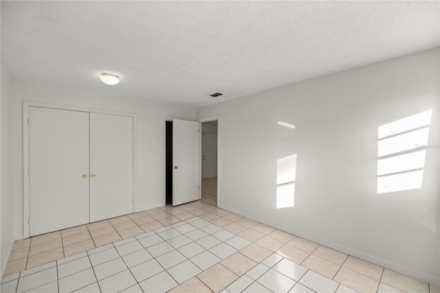 unfurnished bedroom featuring a textured ceiling, a closet, and light tile patterned floors