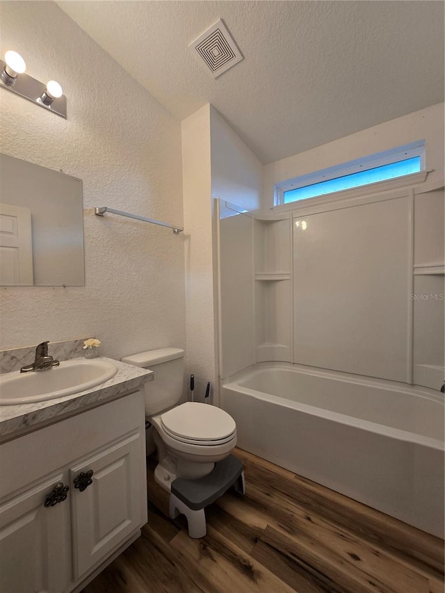 full bathroom featuring washtub / shower combination, toilet, wood-type flooring, a textured ceiling, and vanity