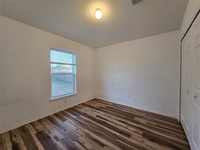 unfurnished bedroom featuring a textured ceiling, dark hardwood / wood-style flooring, and a closet