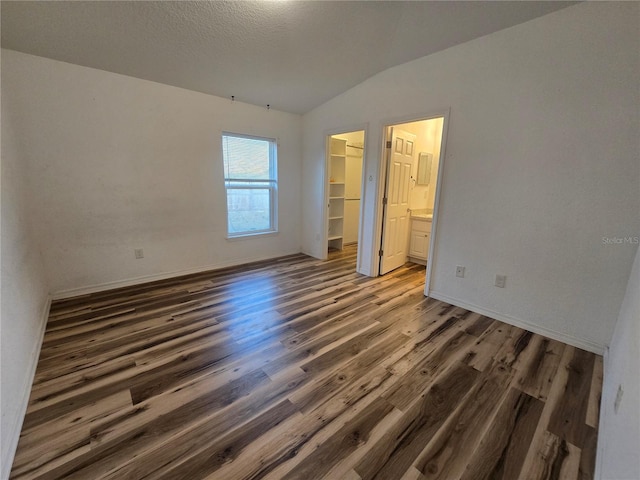 unfurnished bedroom with lofted ceiling, ensuite bath, a spacious closet, dark hardwood / wood-style flooring, and a closet