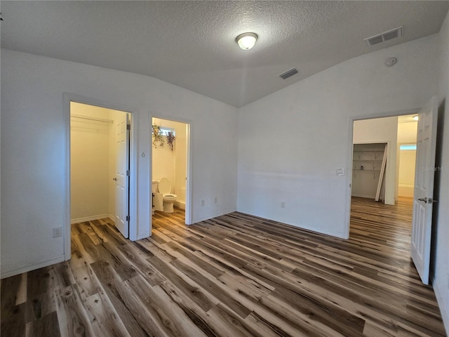 unfurnished bedroom with vaulted ceiling, ensuite bathroom, dark hardwood / wood-style floors, a walk in closet, and a textured ceiling