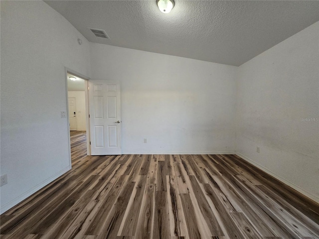 spare room featuring lofted ceiling, dark hardwood / wood-style floors, and a textured ceiling